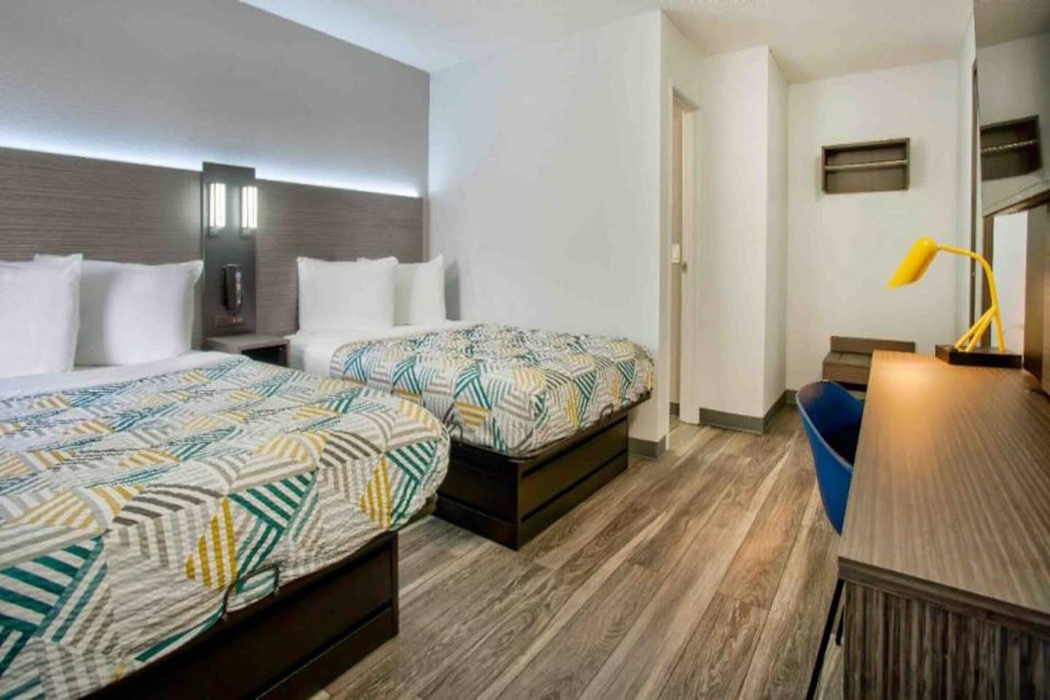 Une chambre d’hôtel avec deux lits, un bureau, une chaise, une lampe et une petite fenêtre.
