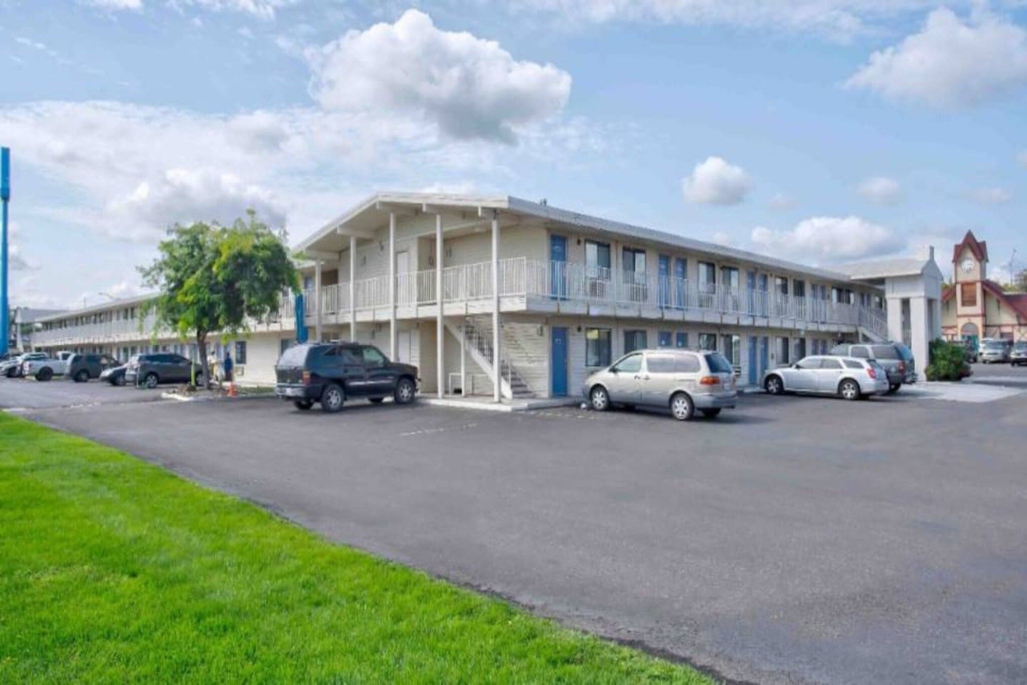 Un motel composé d’un bâtiment à deux étages, d’un parking où sont garées plusieurs voitures et d’une zone herbeuse en premier plan.