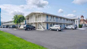 Un motel composé d’un bâtiment à deux étages, d’un parking où sont garées plusieurs voitures et d’une zone herbeuse en premier plan.