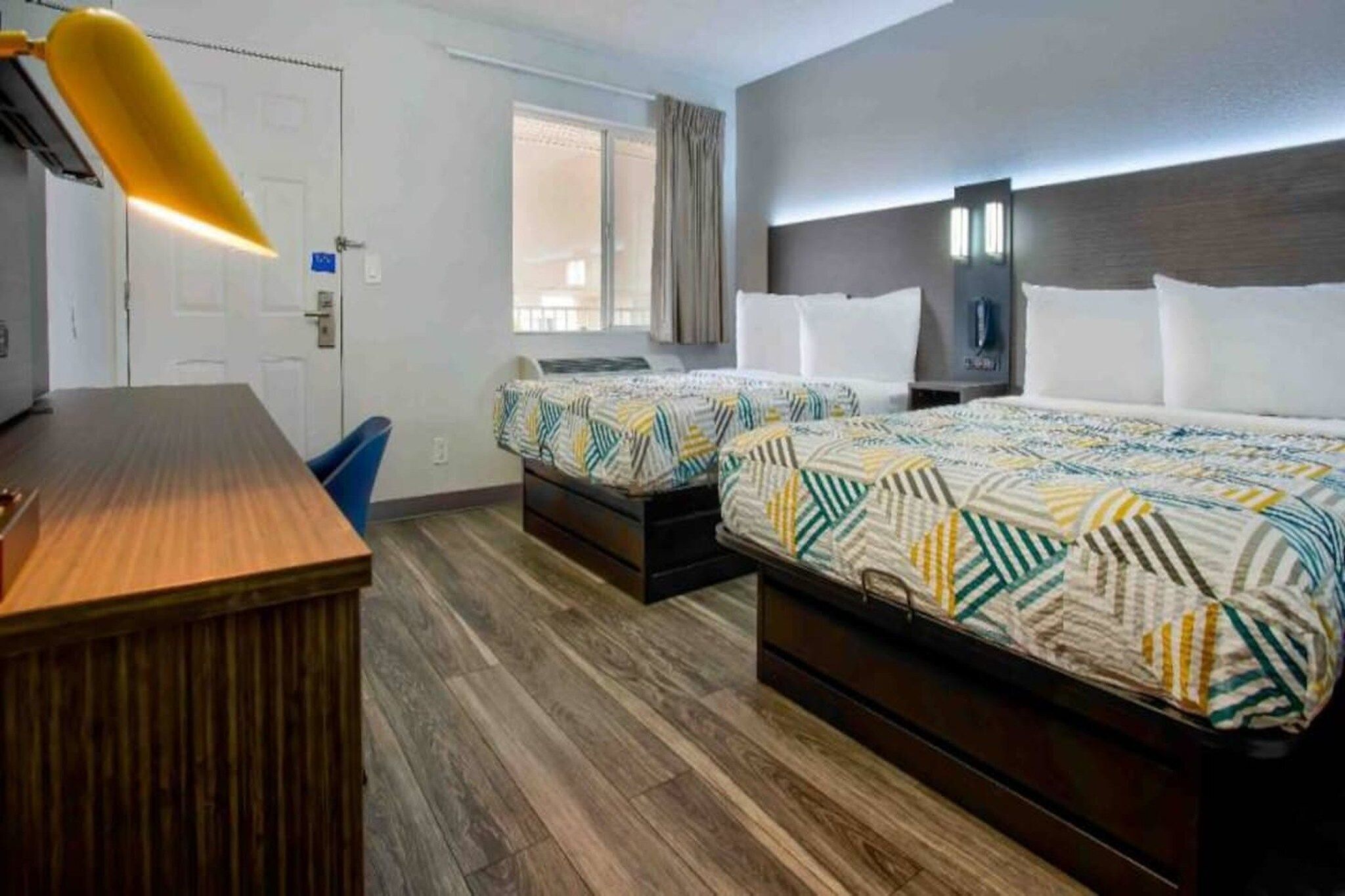 A hotel room with two beds, a desk, a chair, and a window with curtains.