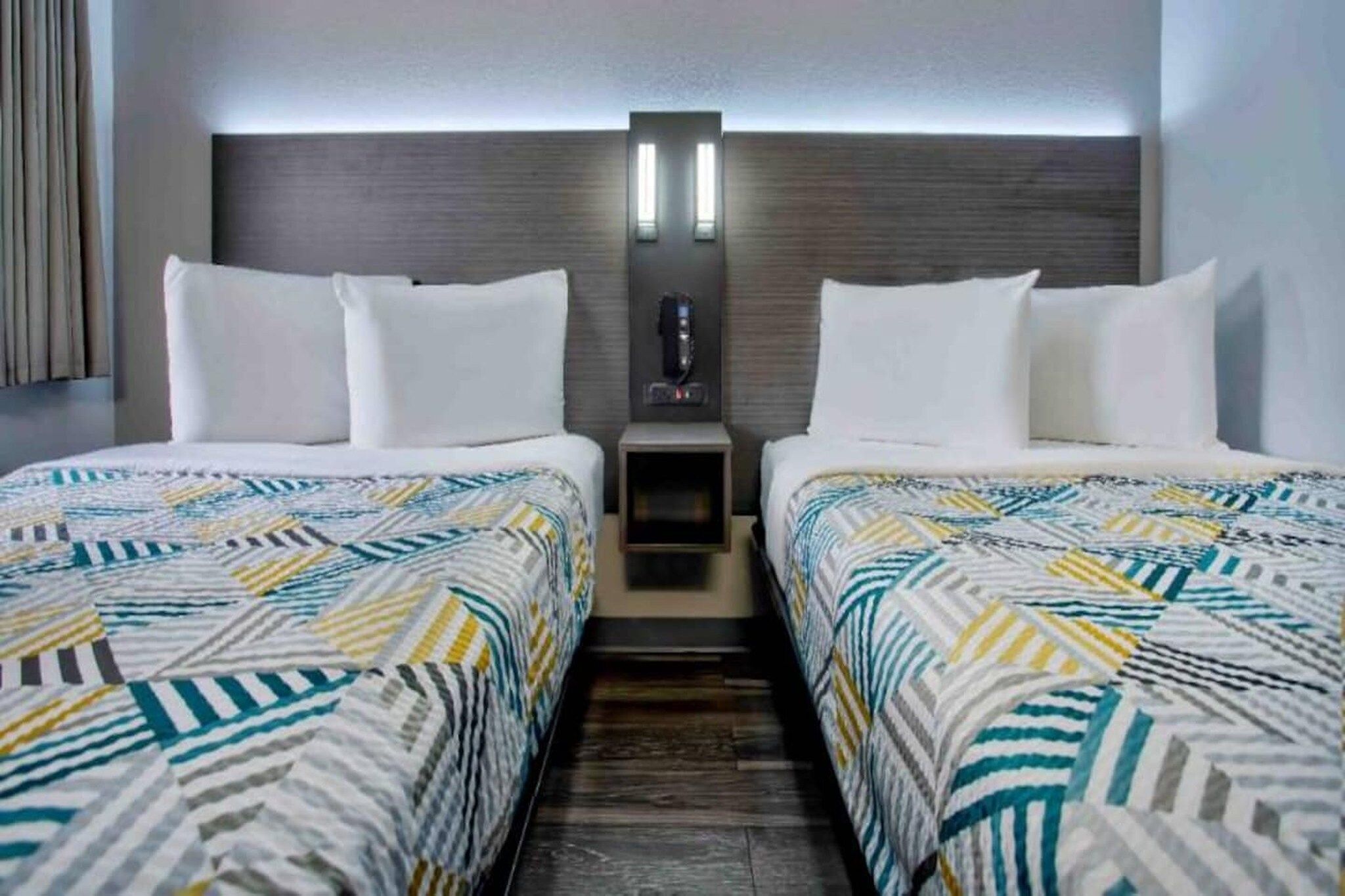 Una habitación de hotel con dos camas, una mesita de noche y una lámpara fijada a la pared.