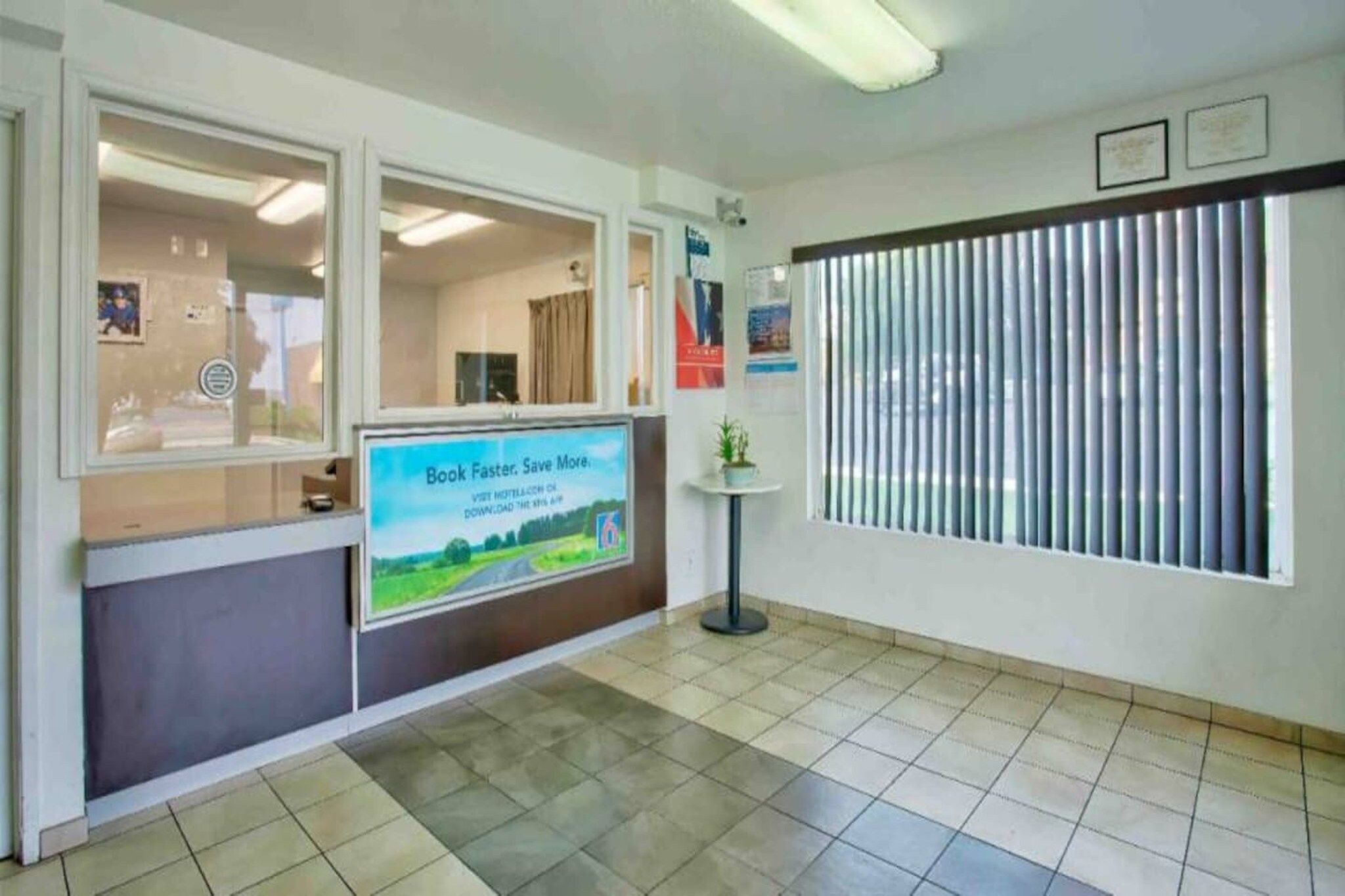 Ein Empfangsbereich mit einem großen Plakat, einem Fenster mit Jalousien und einem Fliesenboden.