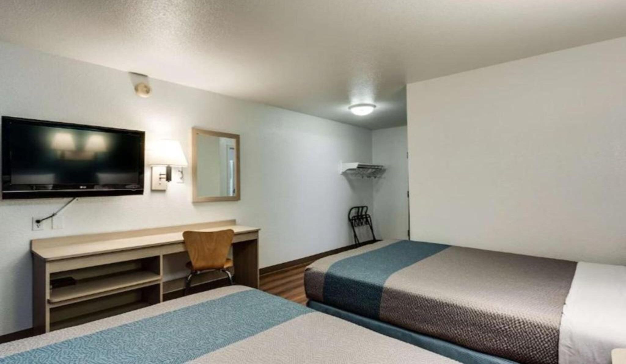 A hotel room with a bed, a desk, a chair, a television, and a mirror.