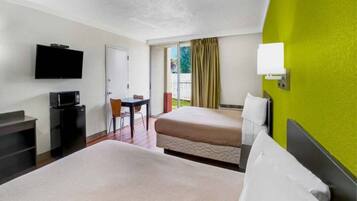 A hotel room with two beds, a desk, a television, and a window with curtains.