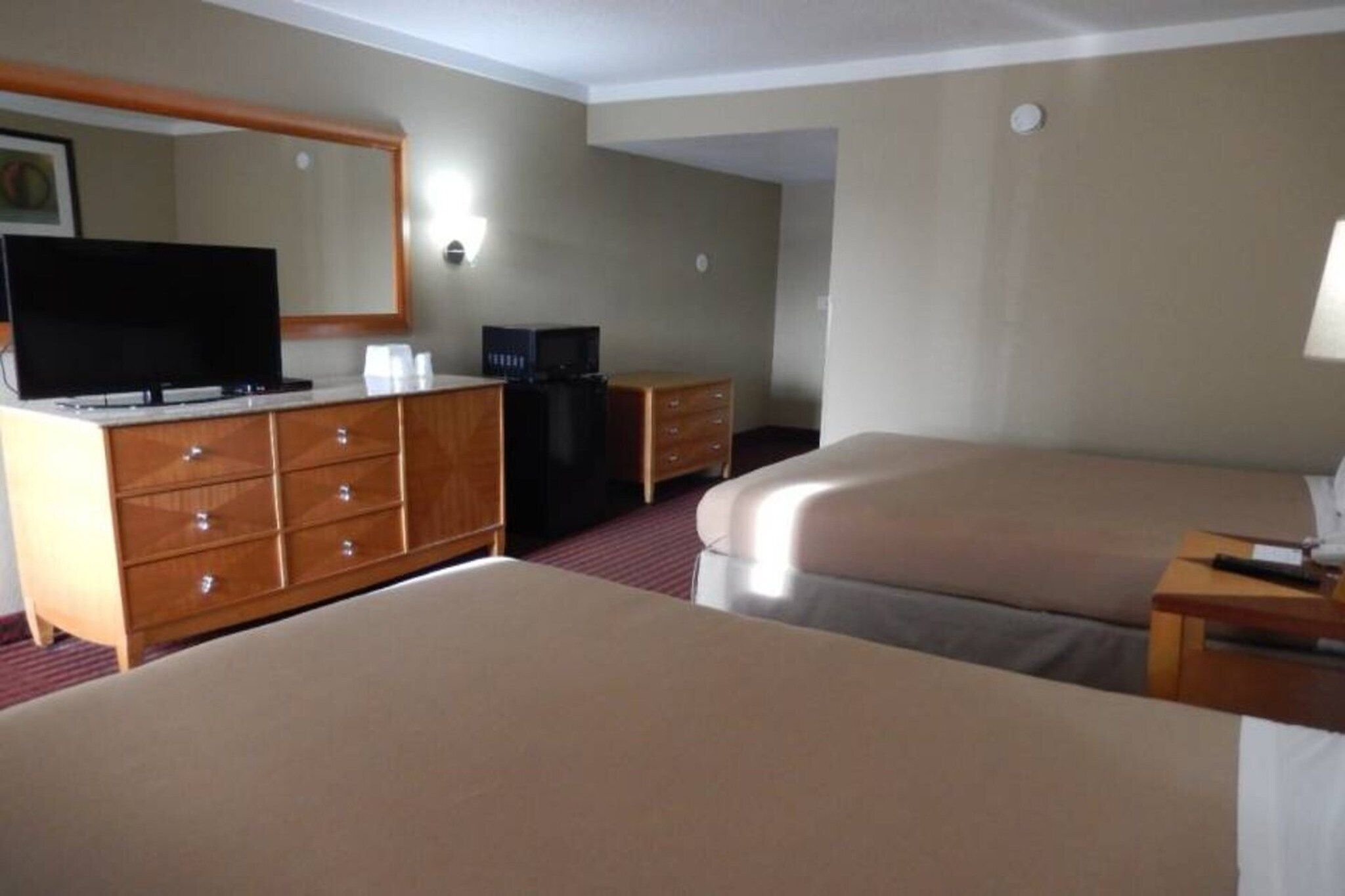A hotel room with two beds, a dresser, a television, and a desk with a lamp.
