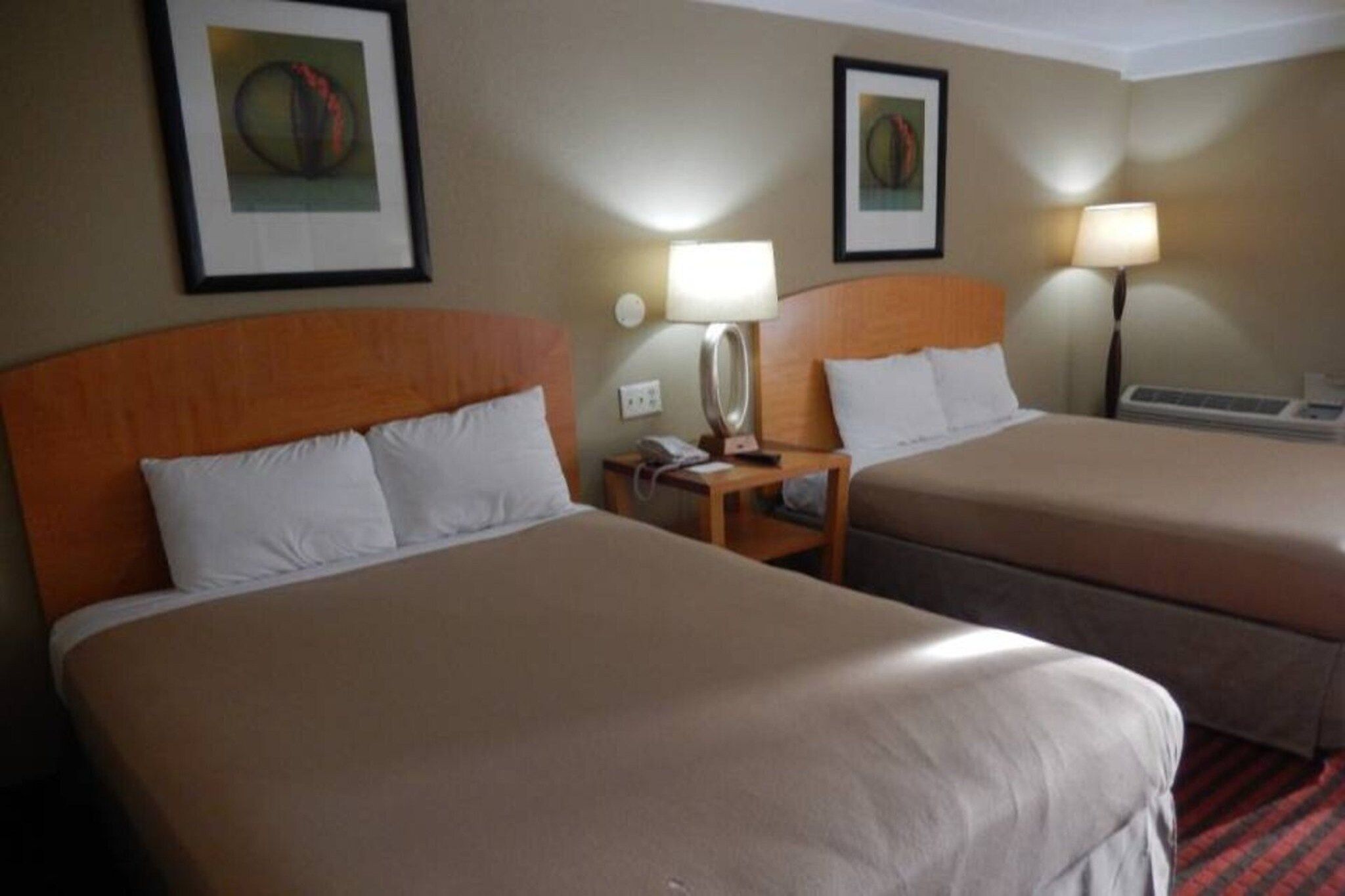 Una camera d'albergo con due letti, un comodino con una lampada e opere d'arte incorniciate al muro.