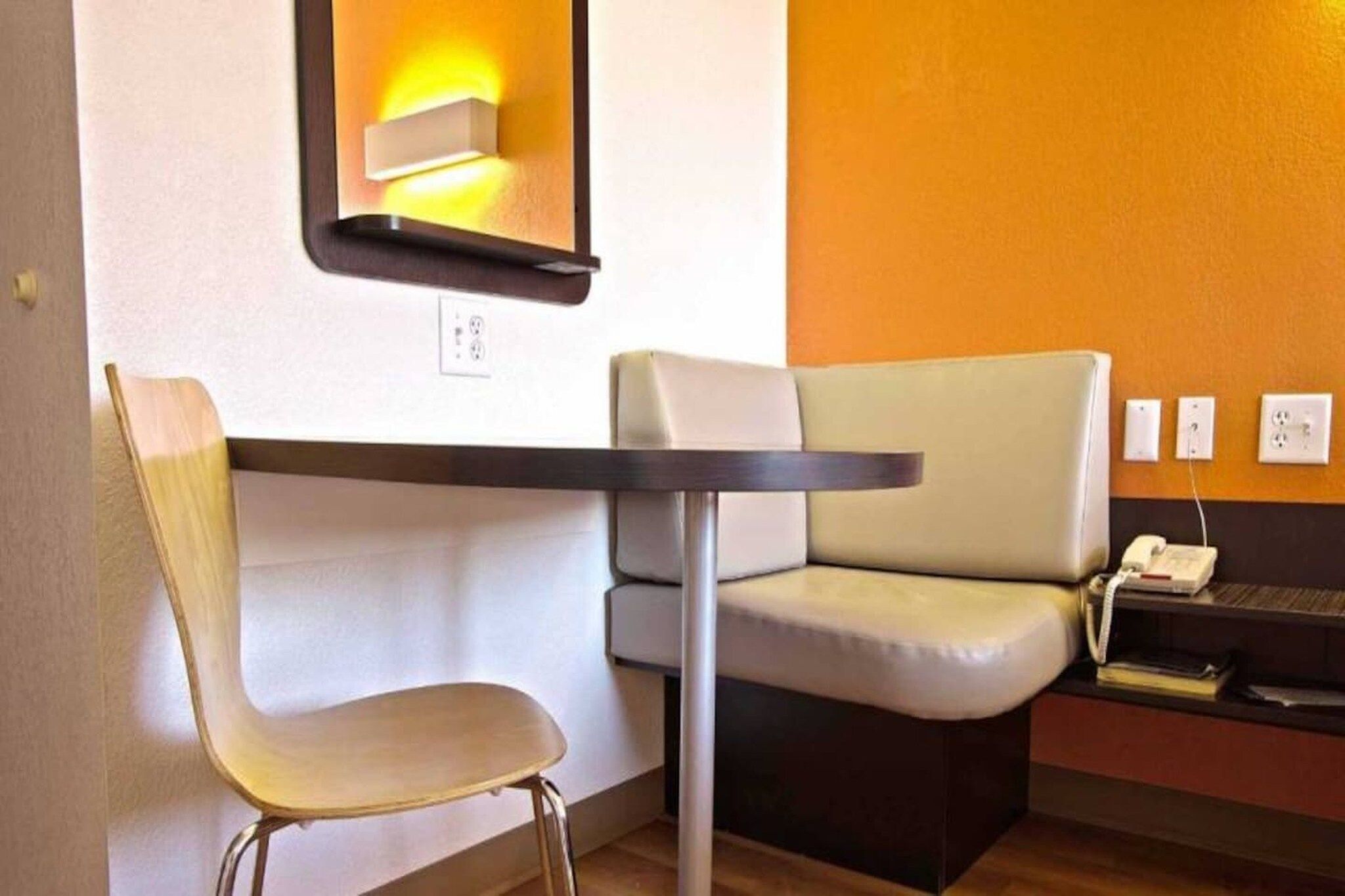 Un rincón con asientos, una mesa, una silla, una lámpara de pared y un teléfono.