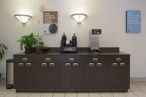 En receptionsdisk med en kaffestation, två väggmonterade lampor och en skylt om möjligheten att ladda sina enheter på morgonen.