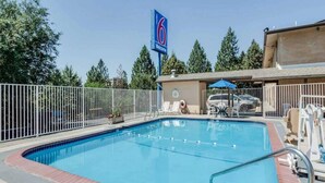 A swimming pool with a fenced area, lounge chairs, and a building with a '6 Welcome' sign. - 2 Full Beds | Smoking, Micfridge (Spokane)
