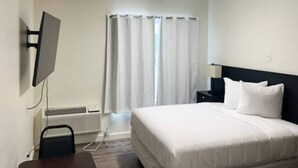 A hotel room with a bed, a TV mounted on the wall, a desk, and a window with curtains. - 1 Queen Bed | Mobil Access Tub Nsmk Kitchen (Pasco)