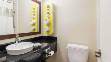 Un baño con lavamanos, espejo, dispensador de toallas y retrete.