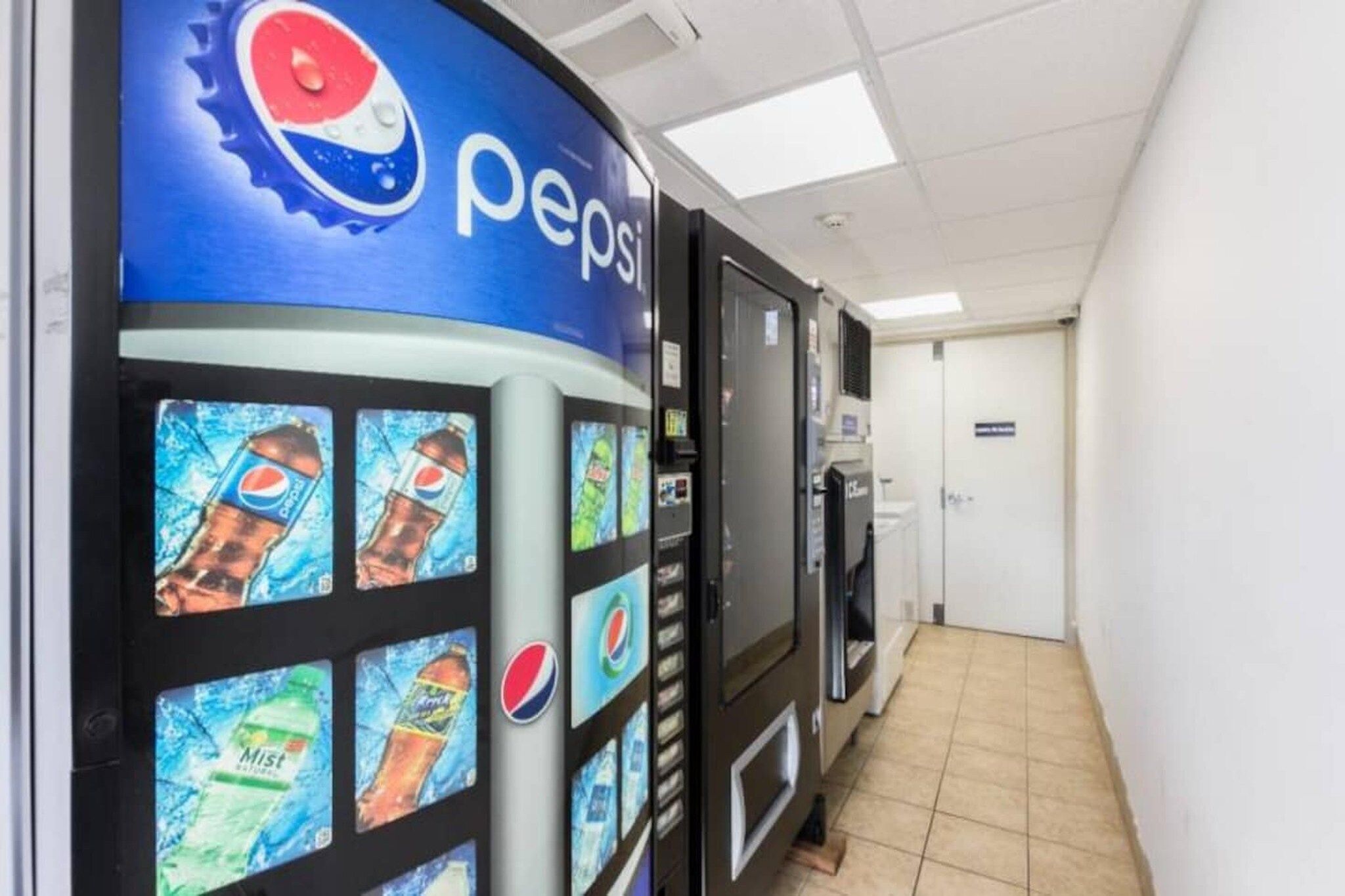 Zona de máquinas expendedoras con la marca Pepsi, piso de baldosas y una puerta al fondo.