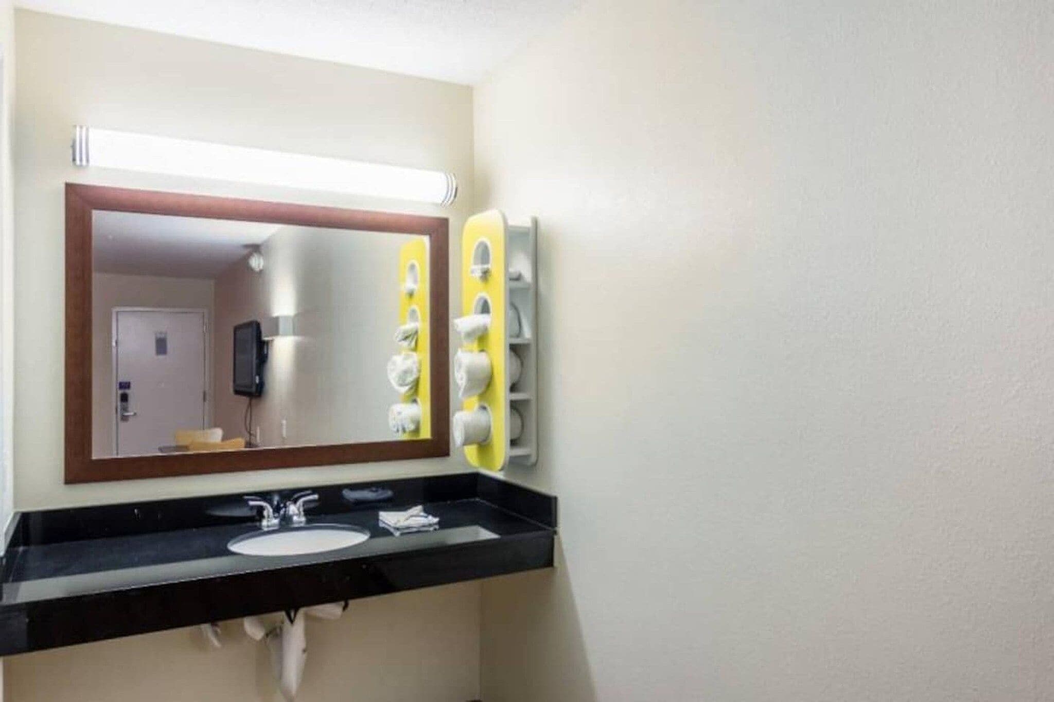 Un baño con espejo, dos lavamanos y dispensador de toallas.