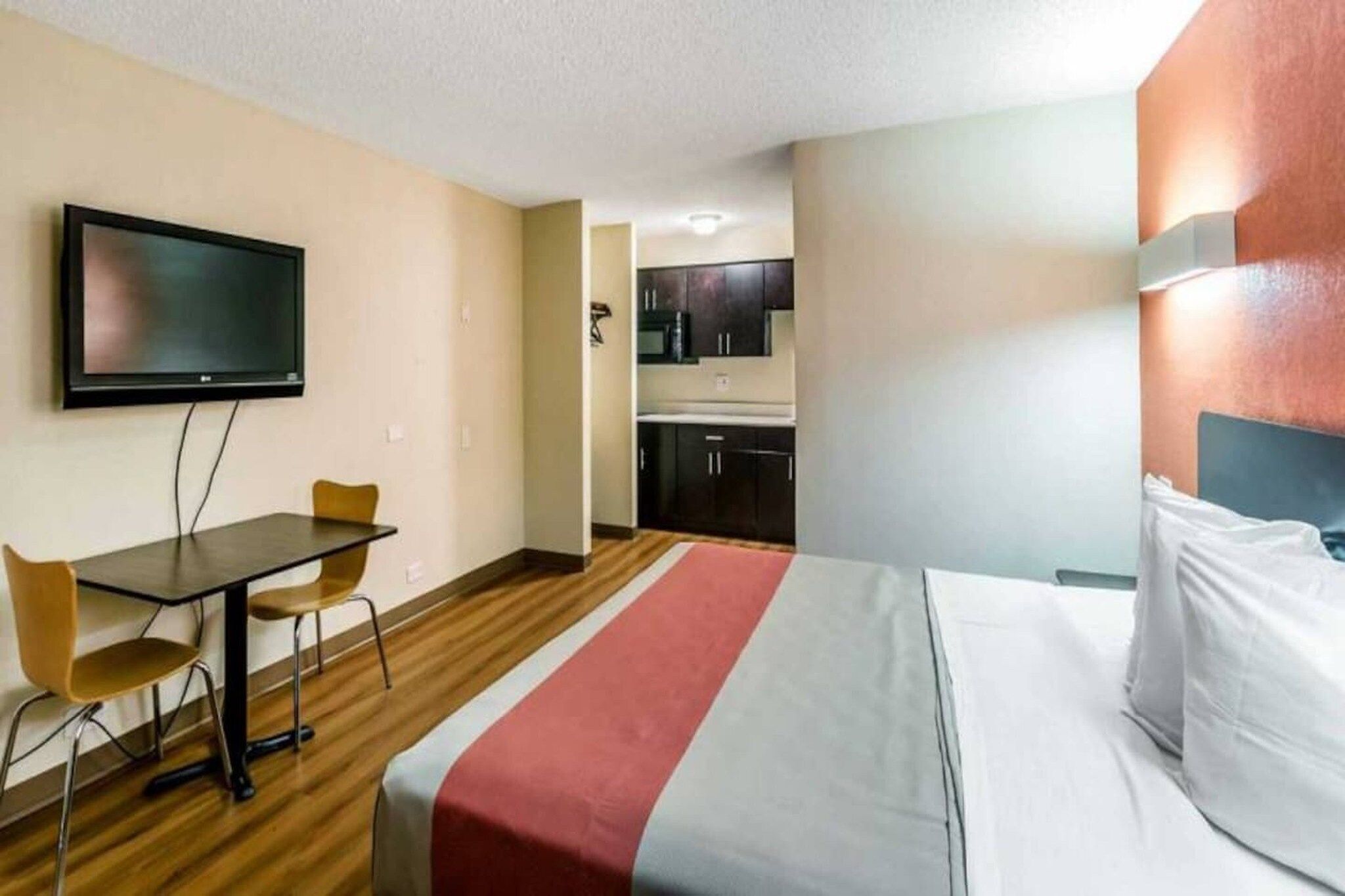 A hotel room with a bed, a desk, a chair, a television, and a kitchenette.