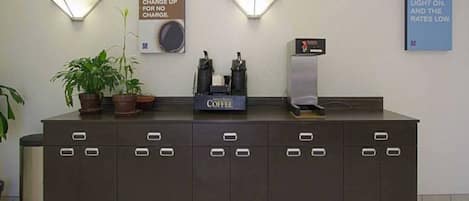 Una recepción con una estación de café, dos lámparas fijadas a la pared y un cartel sobre cargos por la mañana.