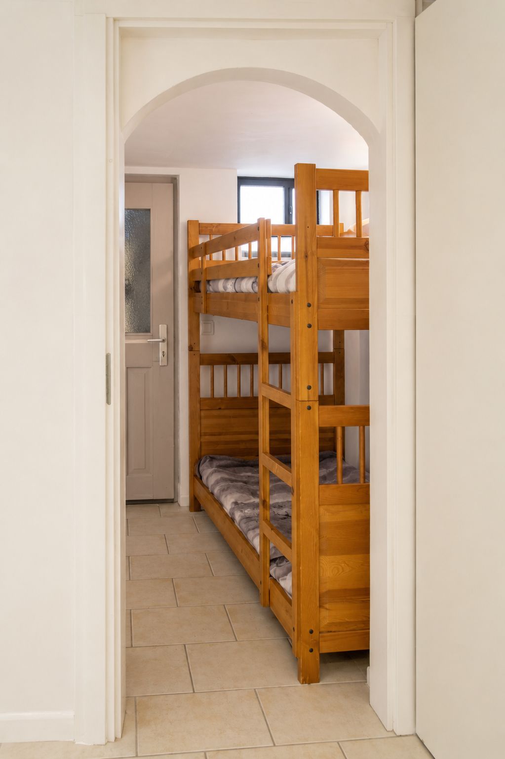Un lit superposé dans un couloir, avec une porte et une fenêtre en arrière-plan.