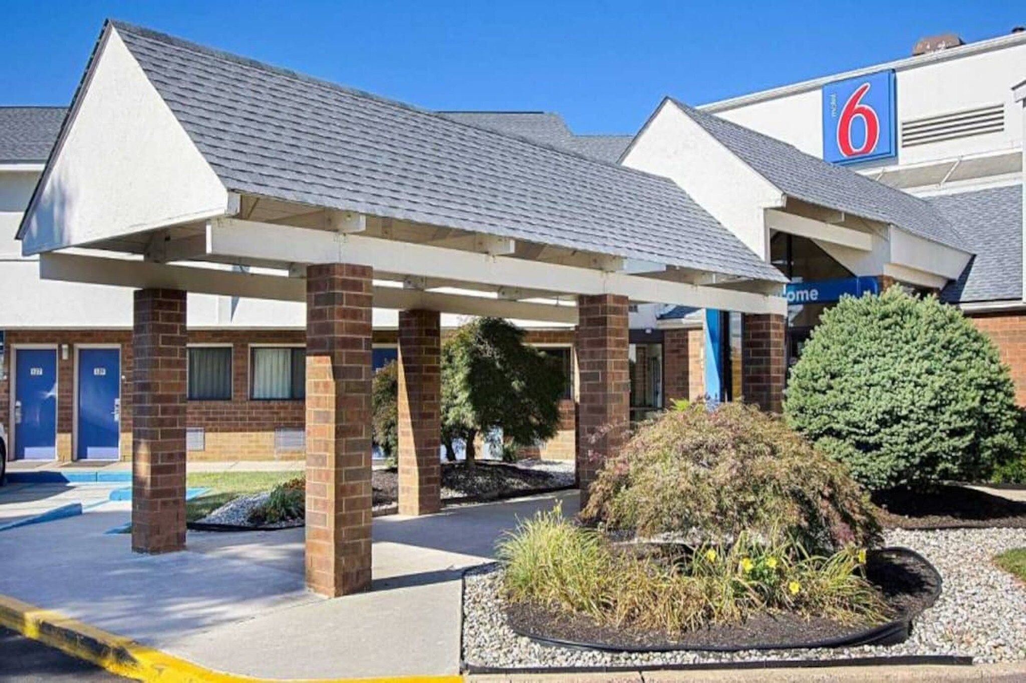 Un hotel con un área exterior techada, estacionamiento y un edificio con un cartel que dice '6'.