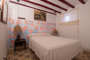 Ein Schlafzimmer mit einem Bett, einer Wand mit Muster, einem Gemälde und einem Fenster mit Jalousien.