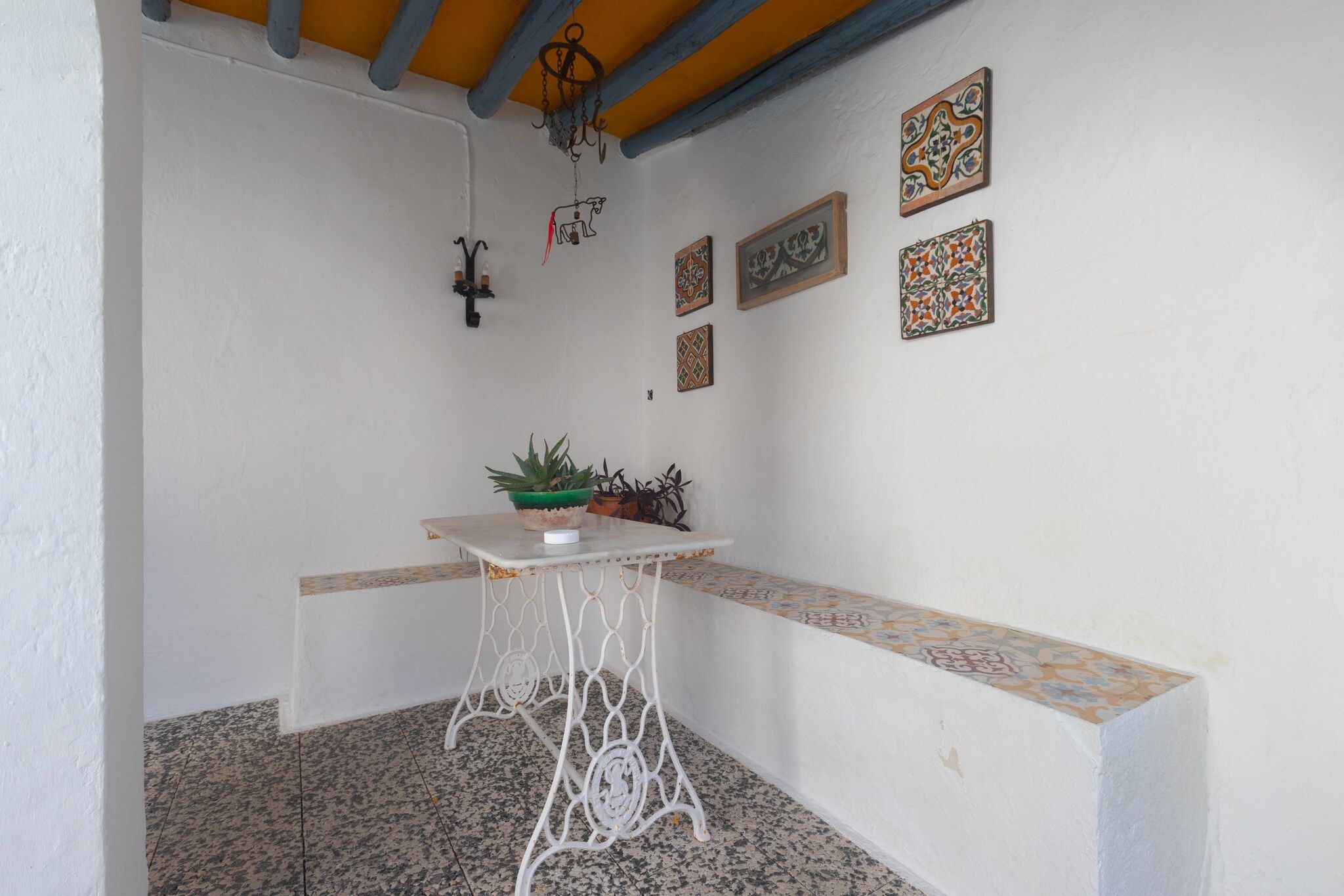 A small, enclosed outdoor area with a white table, potted plants, and decorative tiles on the walls.