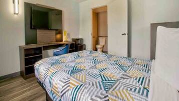 A hotel room with a bed, a desk with a chair, a television, and a toilet.