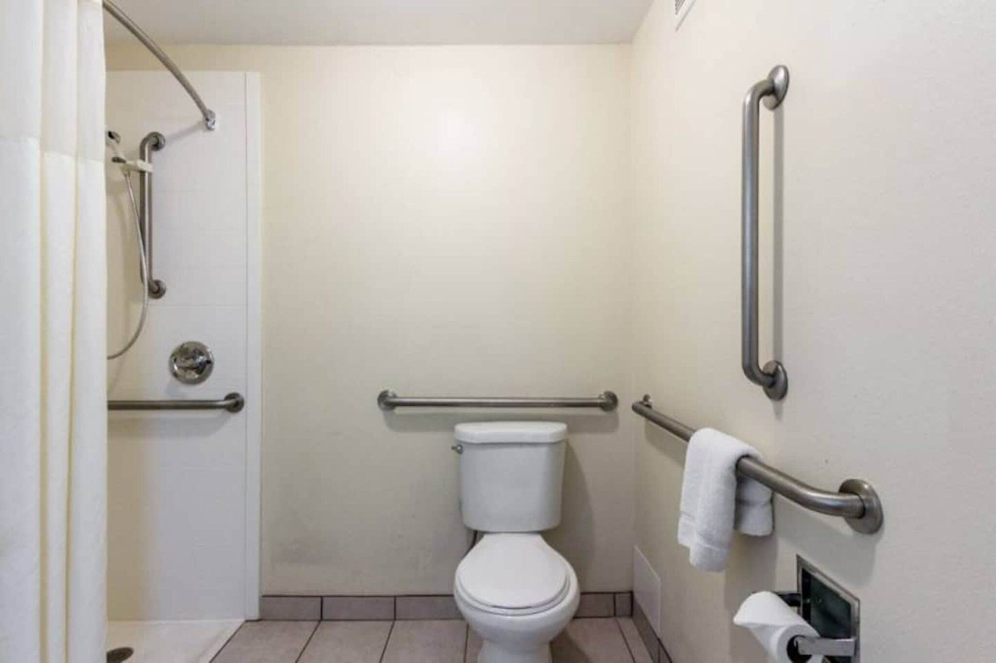 Un baño con inodoro, barras de apoyo, zona de ducha y un perchero para toallas.