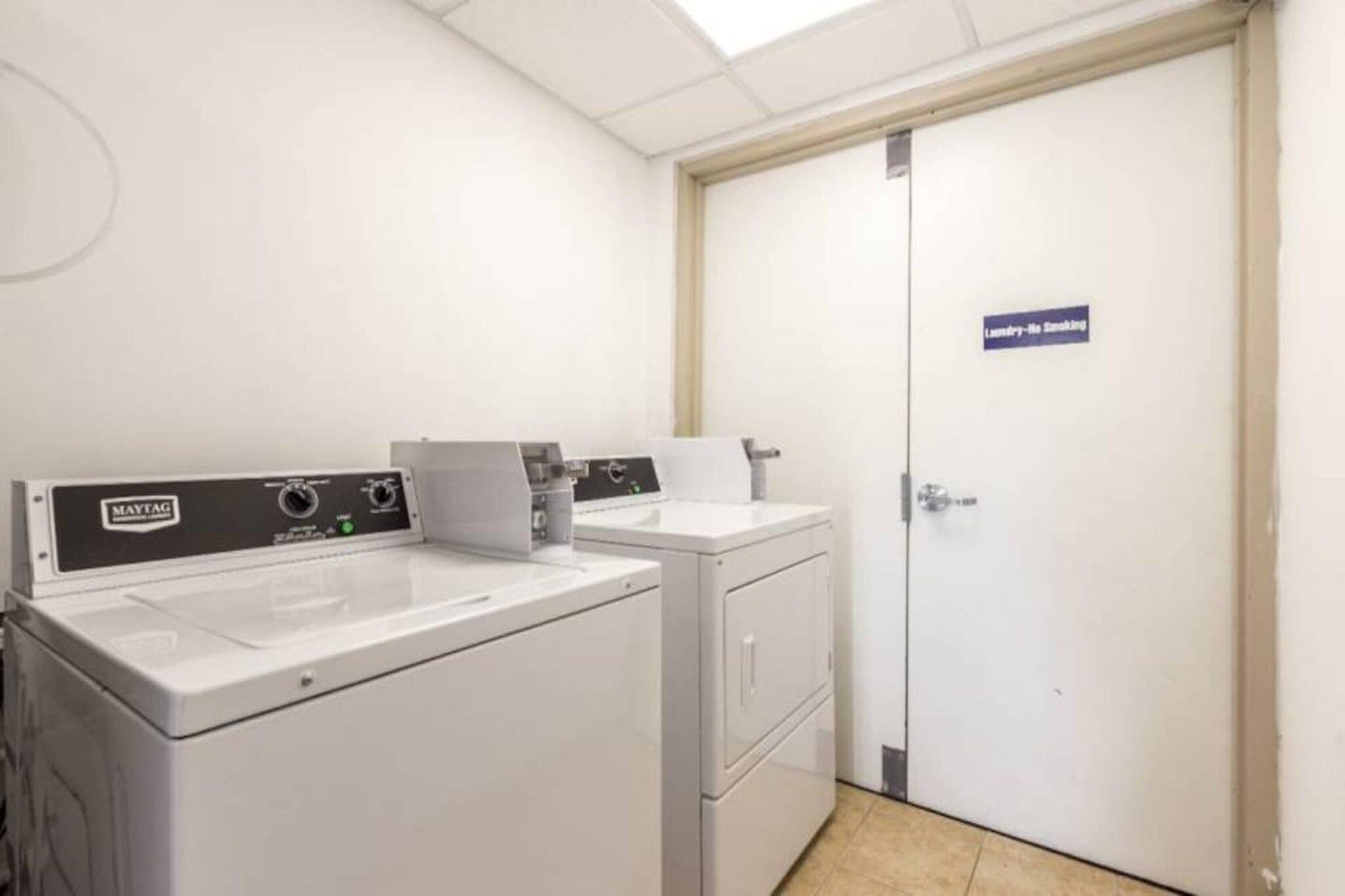 Un cuarto de lavado con lavadora y secadora Maytag, un lavamanos blanco y una puerta con la leyenda 'Cuarto de Lavado'.