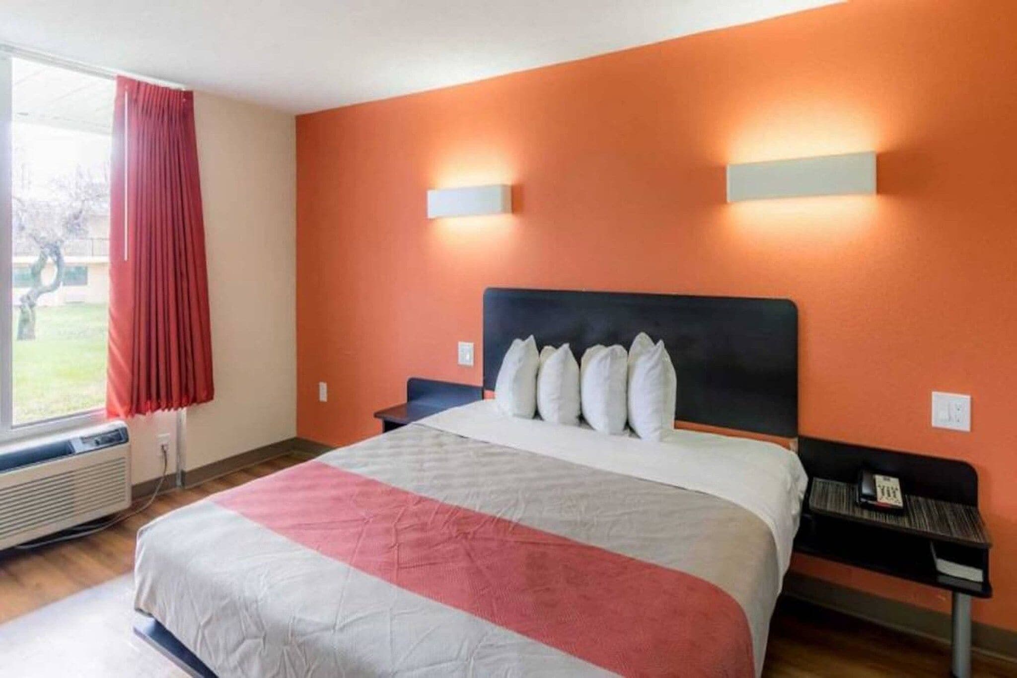Habitación de hotel con una cama grande, una ventana con cortinas rojas y una lámpara de pared.