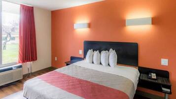 Habitación de hotel con una cama grande, una ventana con cortinas rojas y una lámpara de pared.