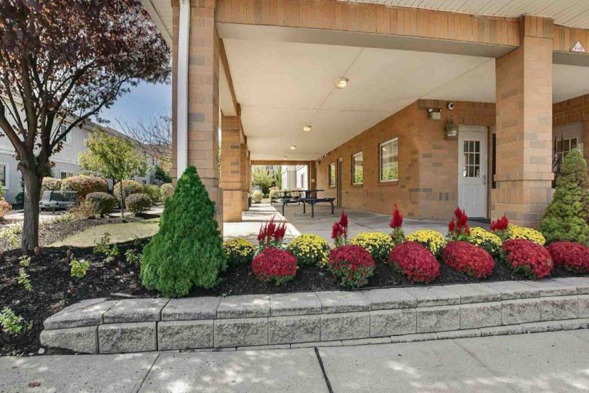 A building with a covered entrance, a stone facade, and a landscaped garden with various shrubs and flowers.