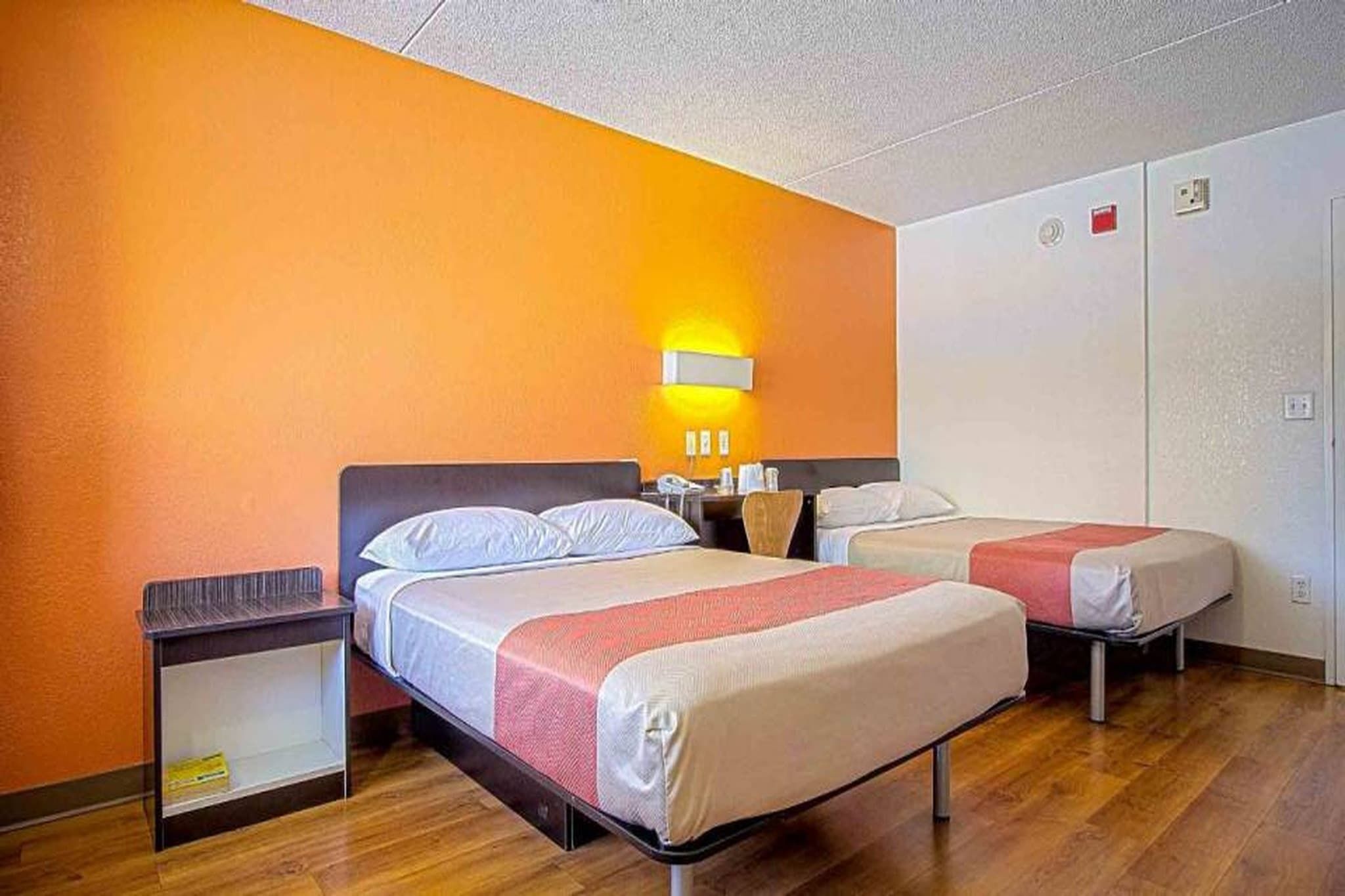 A hotel room with two beds, a nightstand, a wall-mounted lamp, and a wardrobe.