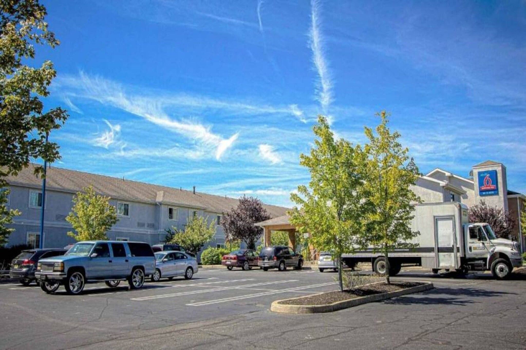 Un estacionamiento con varios vehículos, un edificio con un letrero y un cielo despejado.