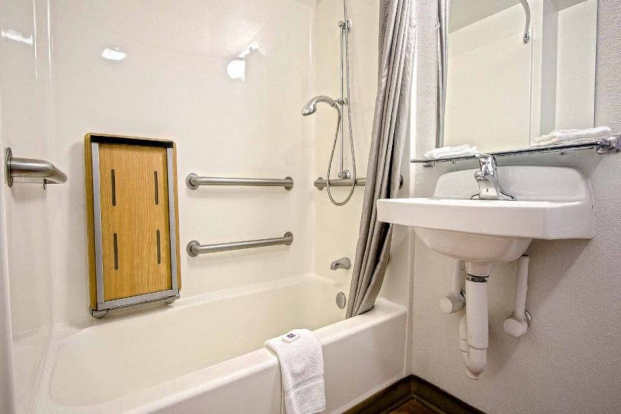 Un bagno con una vasca, un pannello in legno, un corrimano, una doccia e un lavandino.