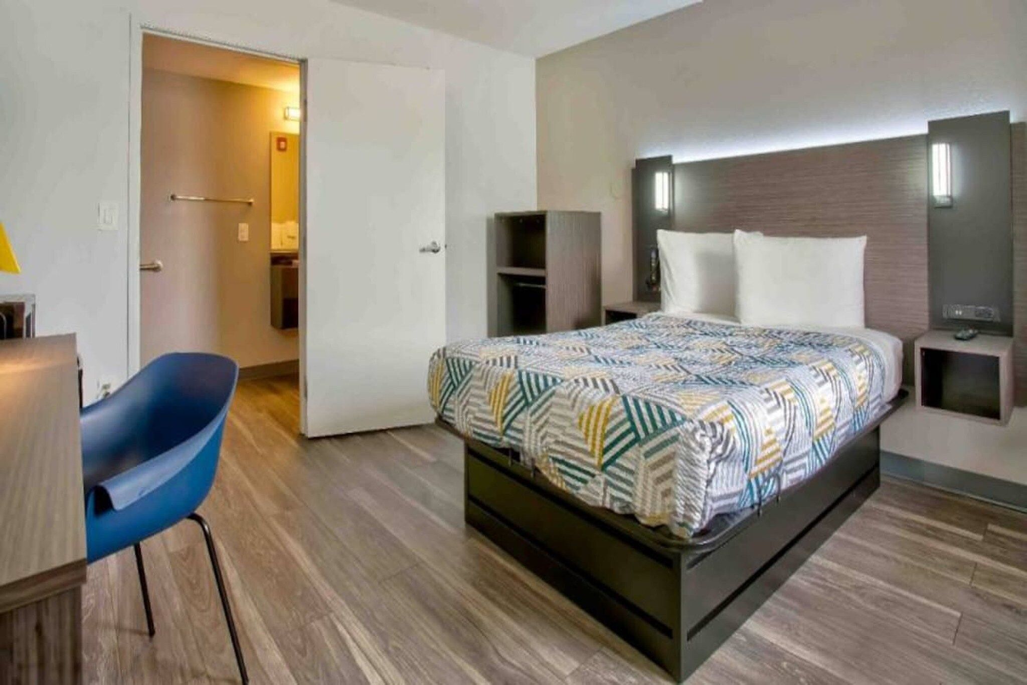 A hotel room with a bed, a desk, a chair, and a wardrobe.