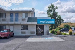 A building with a 'welcome' sign, a parking lot, and a red car parked in front.