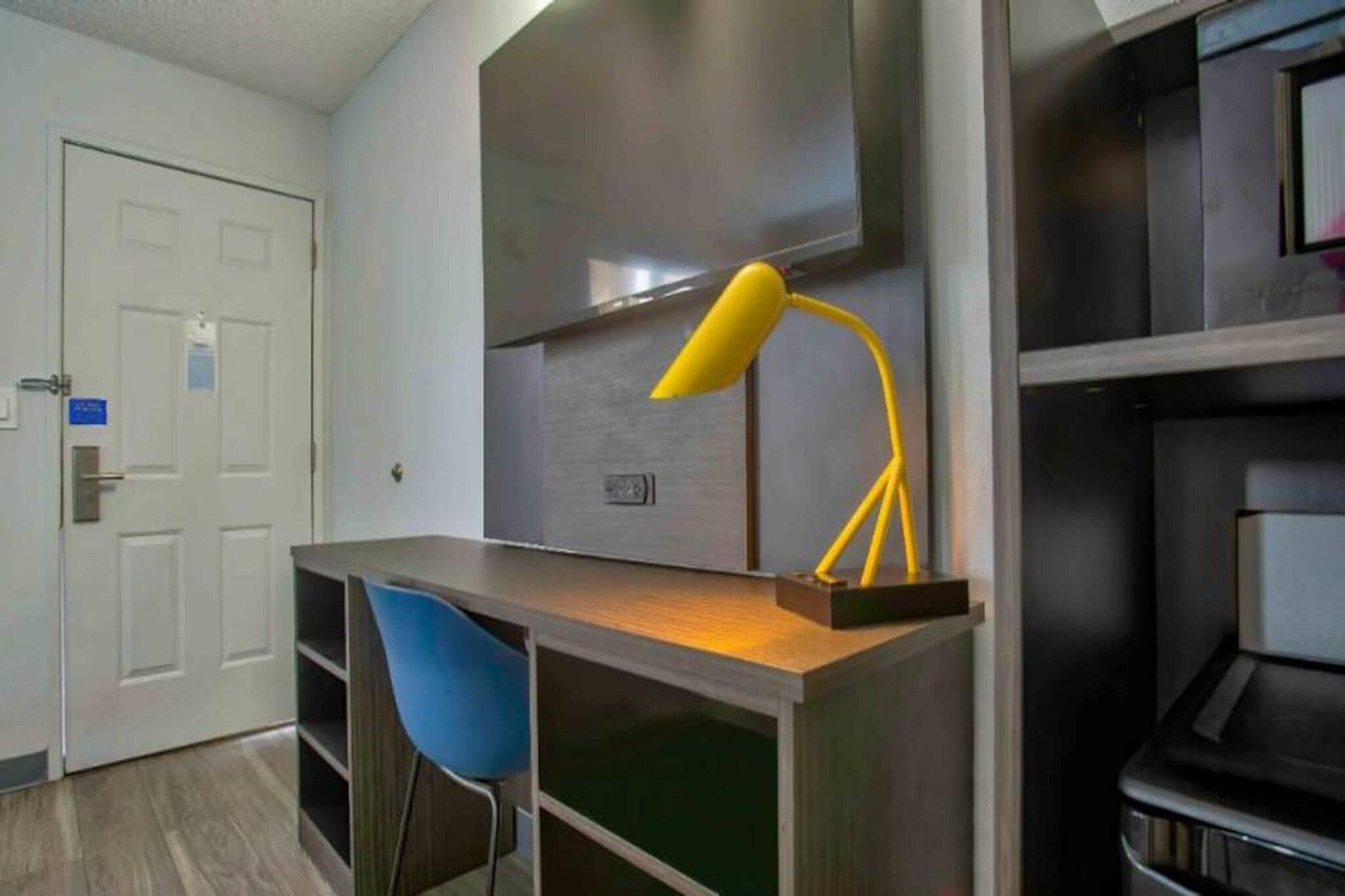 A room with a desk, a chair, a lamp, and a door.