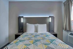 Ein Hotelzimmer mit einem Bett, zwei Nachttischen, einer Wandleuchte und einem Fenster mit Vorhängen.
