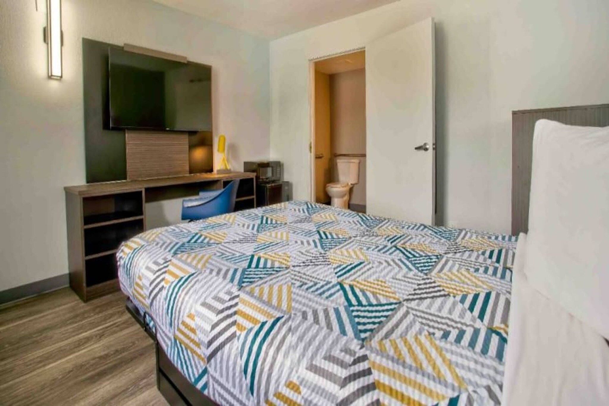 A hotel room with a bed, a desk with a chair, a television, and a toilet.