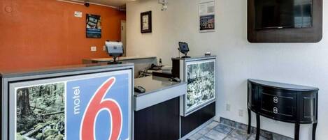 A motel lobby with reception desks, a TV, and a sign indicating the motel number.