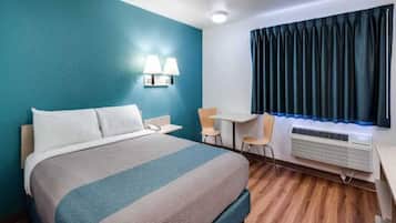 A hotel room with a bed, desk, chairs, and an air conditioning unit.