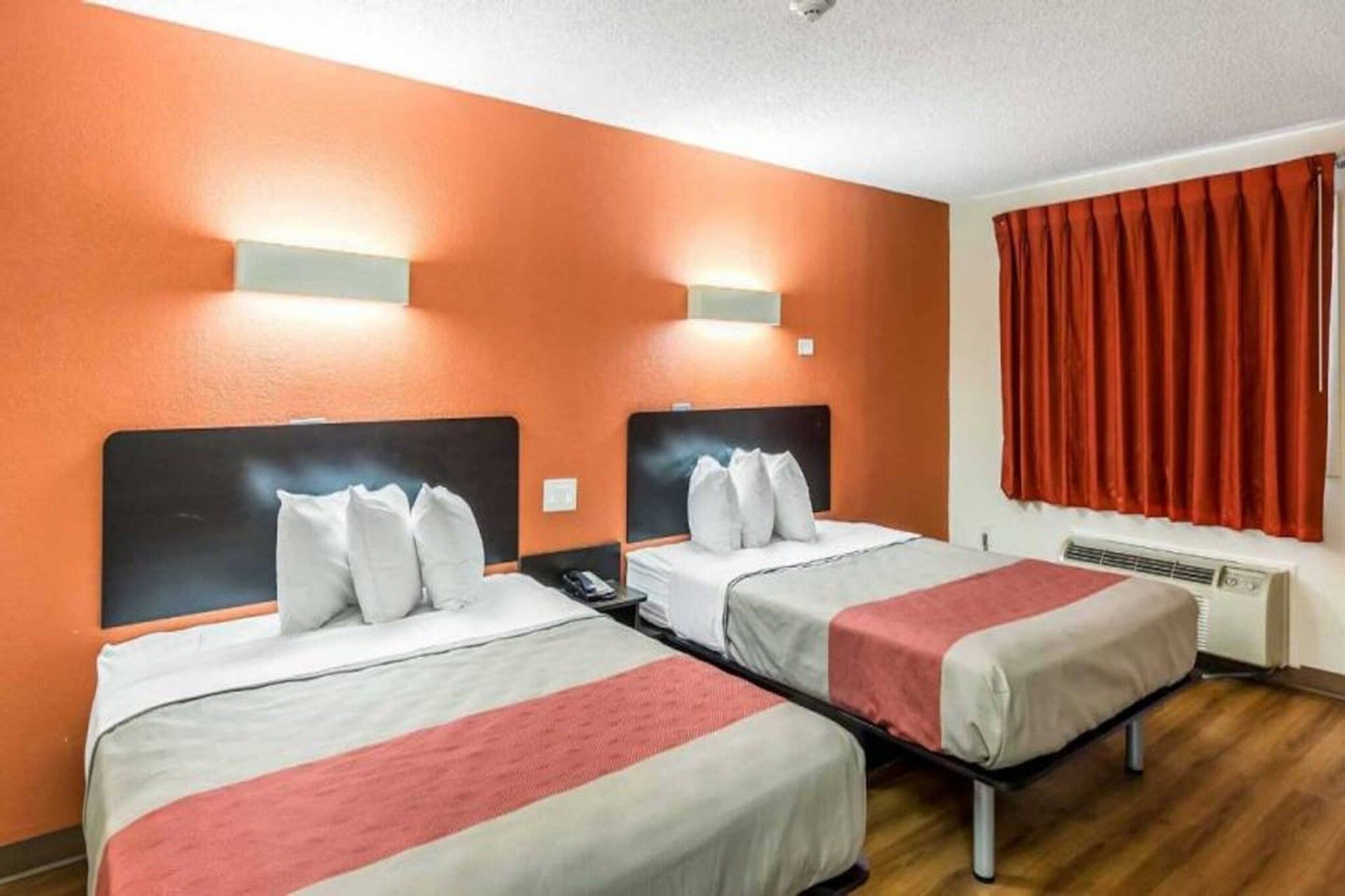 A hotel room with two beds, a red curtain, and a wall-mounted heater.