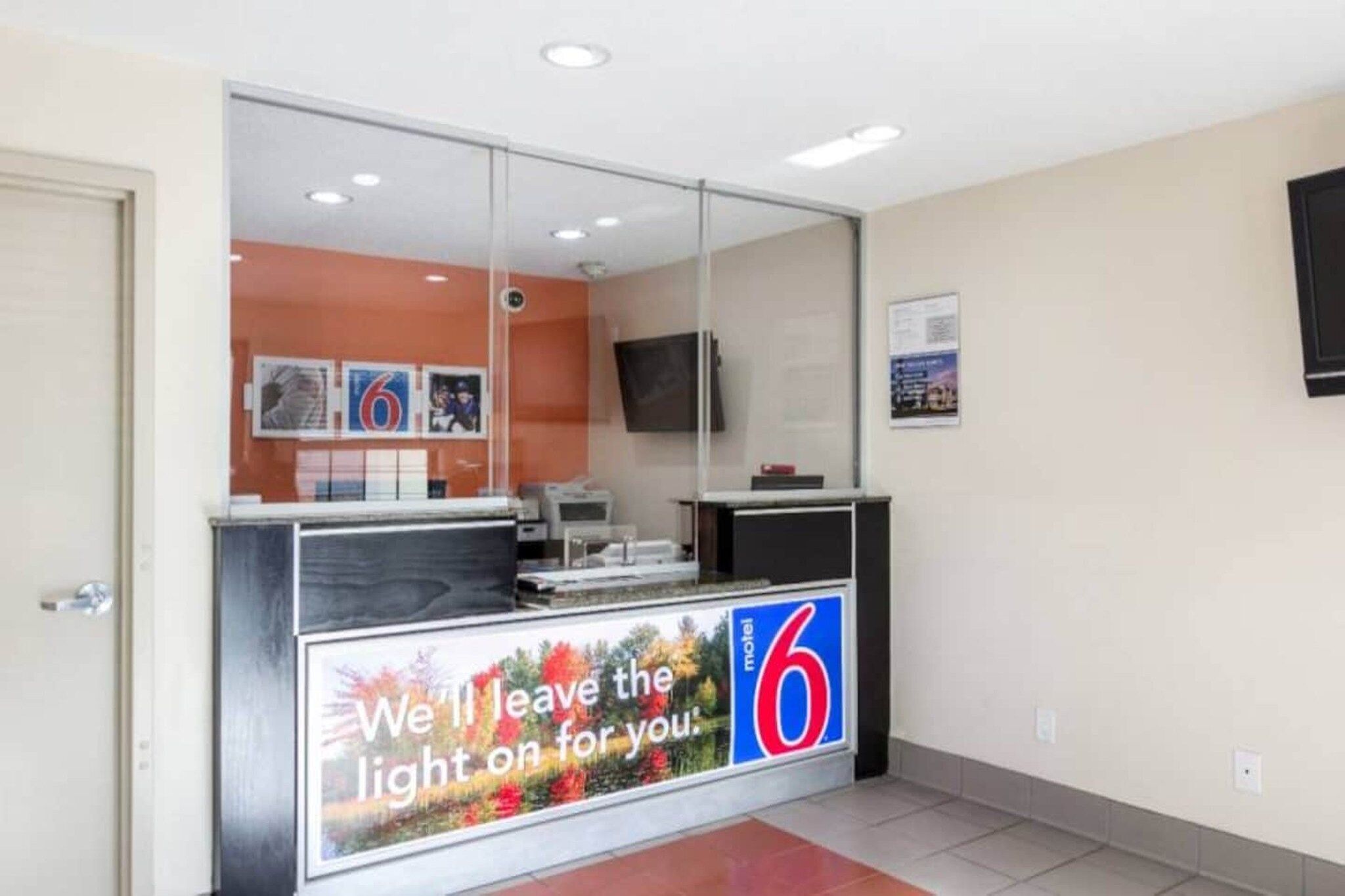 A reception area with a glass partition, a digital display board, and a flat-screen TV mounted on the wall.