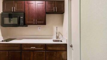 A kitchen with dark wooden cabinets, a microwave, a sink, and a door.
