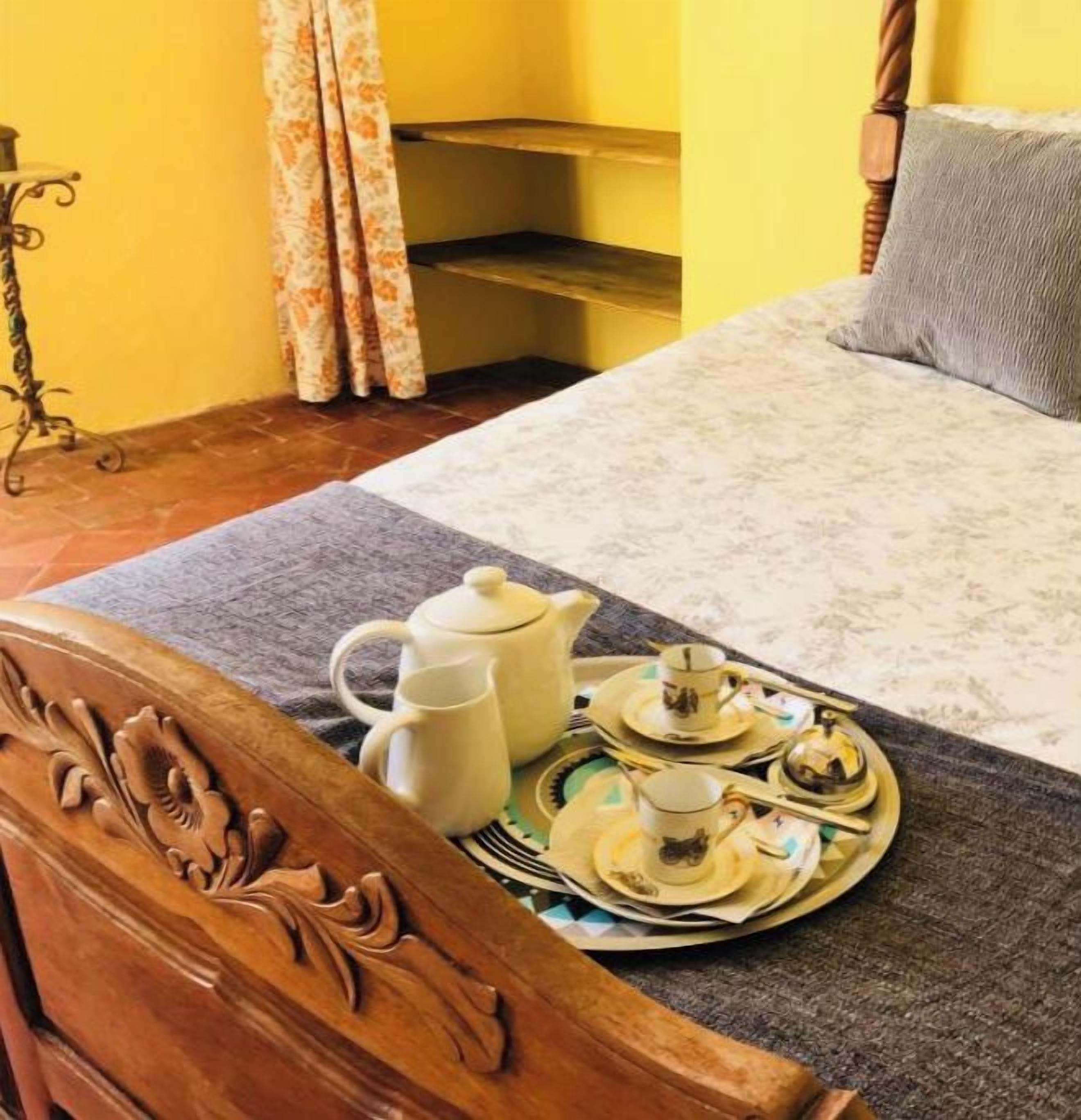 A neatly made bed with a grey pillow, a wooden headboard, and a tray with tea set on a grey bedspread.