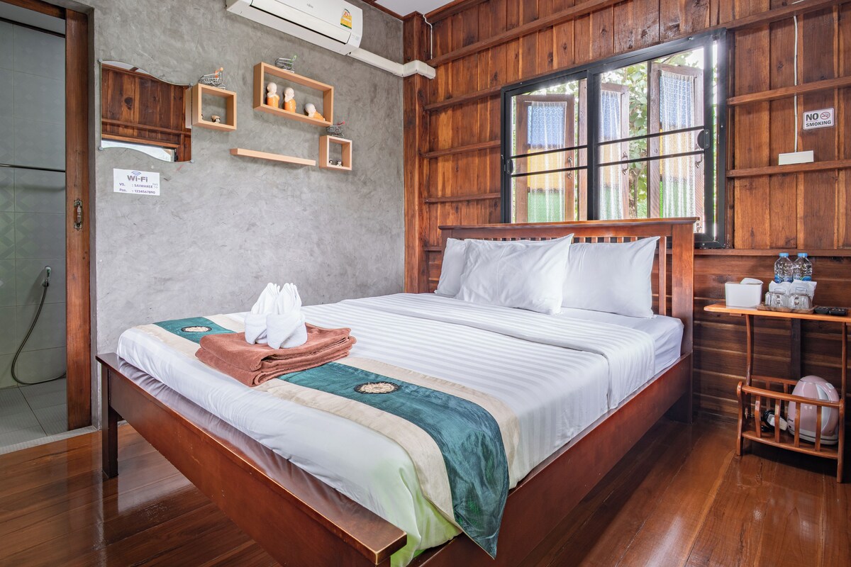 A wooden-framed room with a bed, a window, a wall-mounted air conditioner, and a sign indicating no smoking.