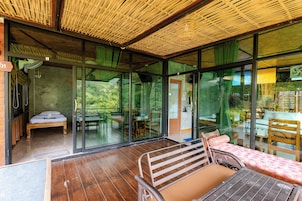 A room with a bed, a table, and a chair, with a view of greenery outside.