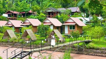 A series of wooden cabins with pitched roofs, surrounded by lush greenery and a river.