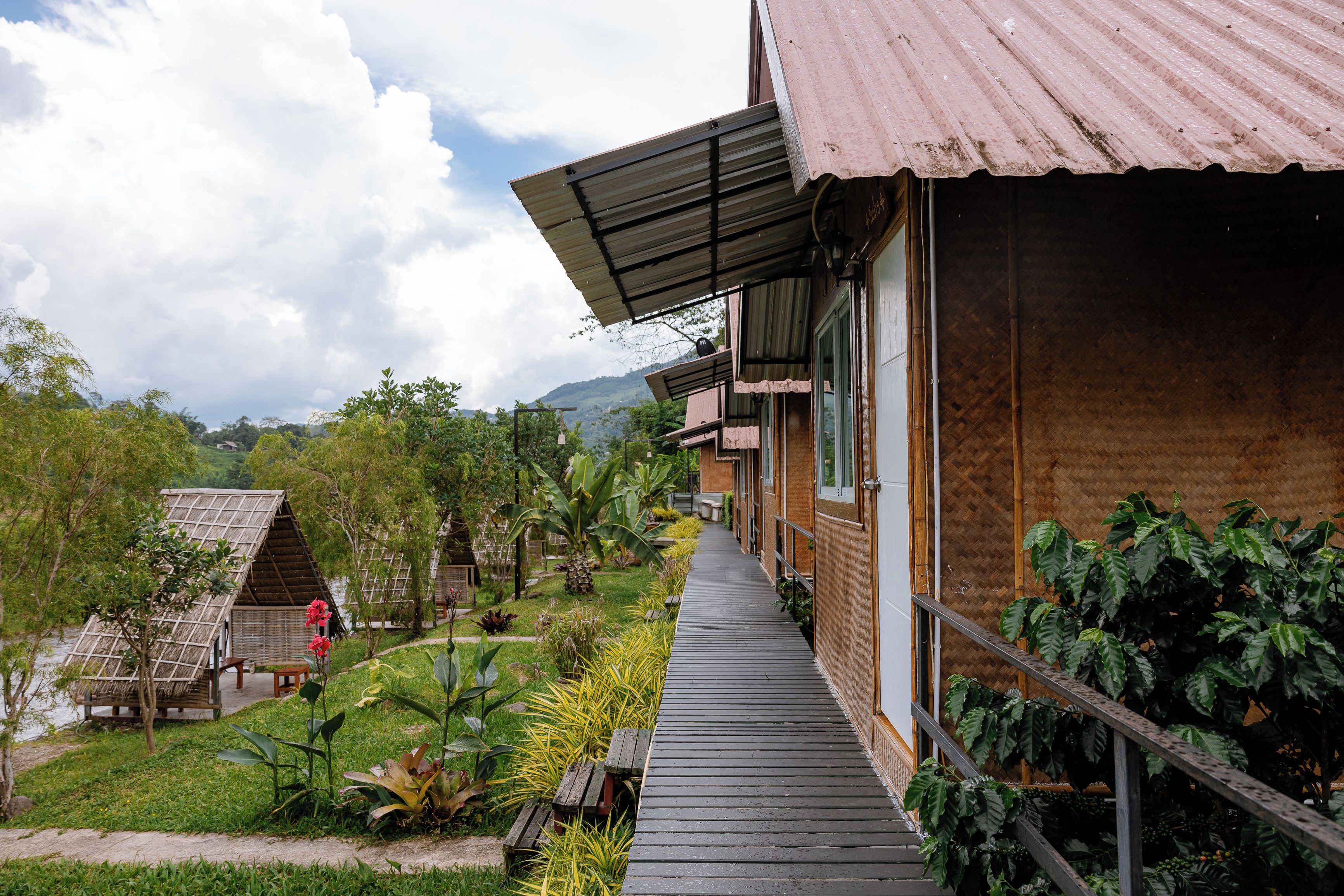 A wooden building with a covered walkway, surrounded by lush greenery and a clear sky.