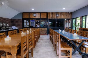 A restaurant with wooden tables and chairs, a brick wall, and a counter with a refrigerator.