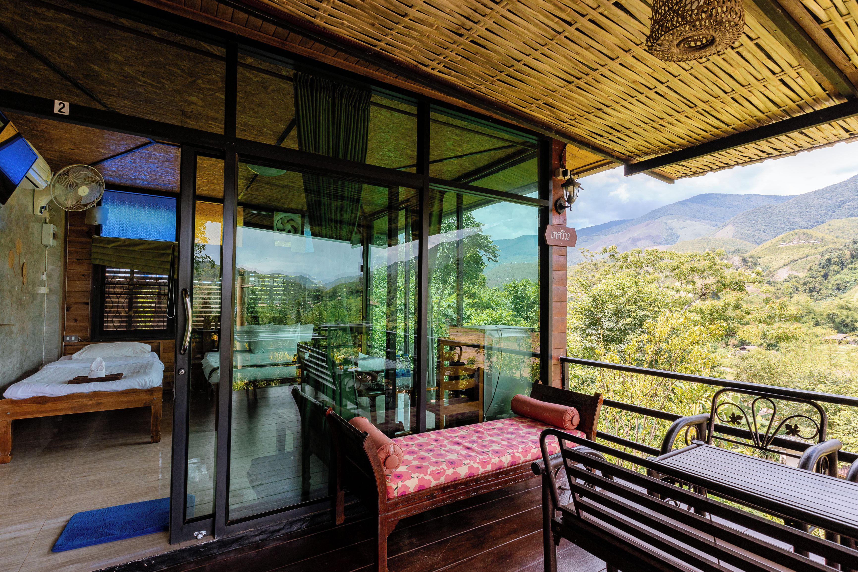 Une chambre dotée d’un mur en verre donnant sur une vue imprenable sur les montagnes, avec un lit en bois, une table et un banc.