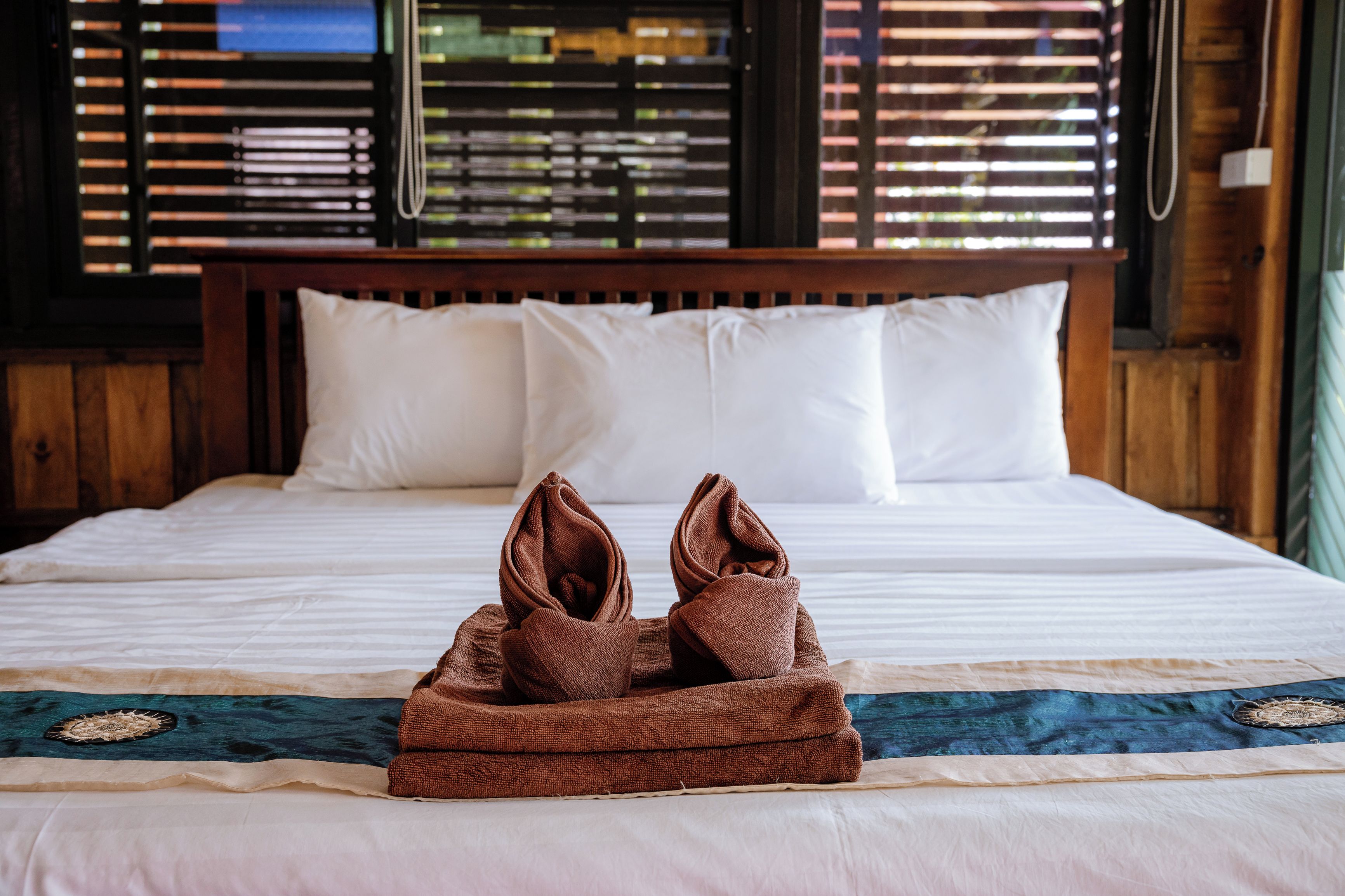 Una cama bien hecha con una toalla marrón doblada encima, almohadas blancas y una colcha estampada.